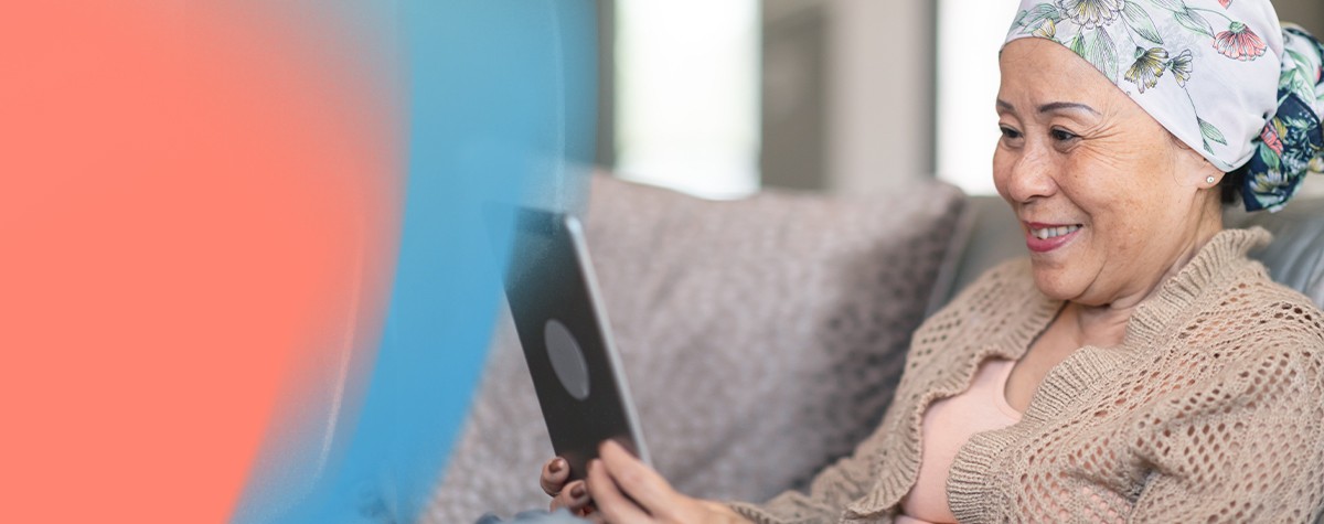 Person wearing a headscarf sits on a couch while using a tablet.